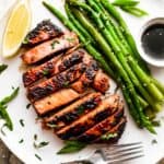 wide overhead shot of a white dinner plate with a sliced tuna steak, asparagus stalks, soy dipping sauce, and a lemon wedge.