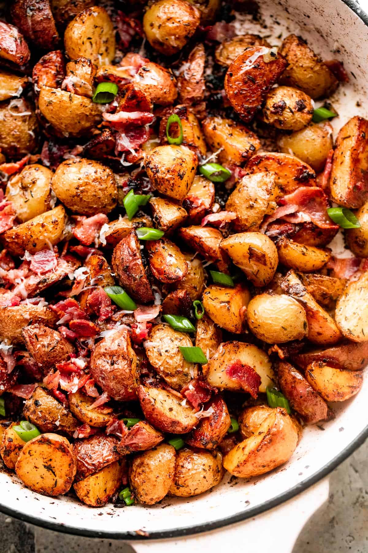 overhead shot of roasted potatoes and bacon in a white skillet.