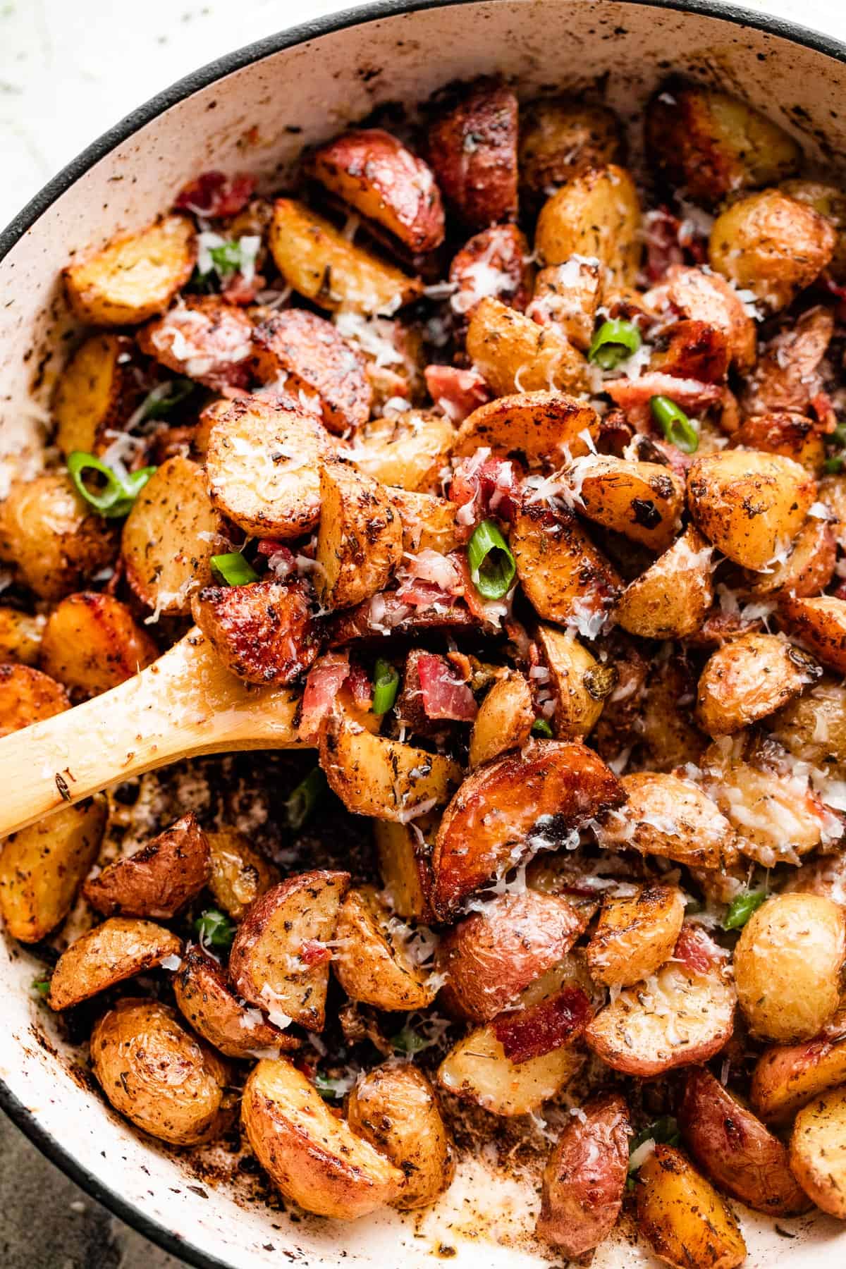 overhead shot of roasted potatoes and bacon in a white skillet.