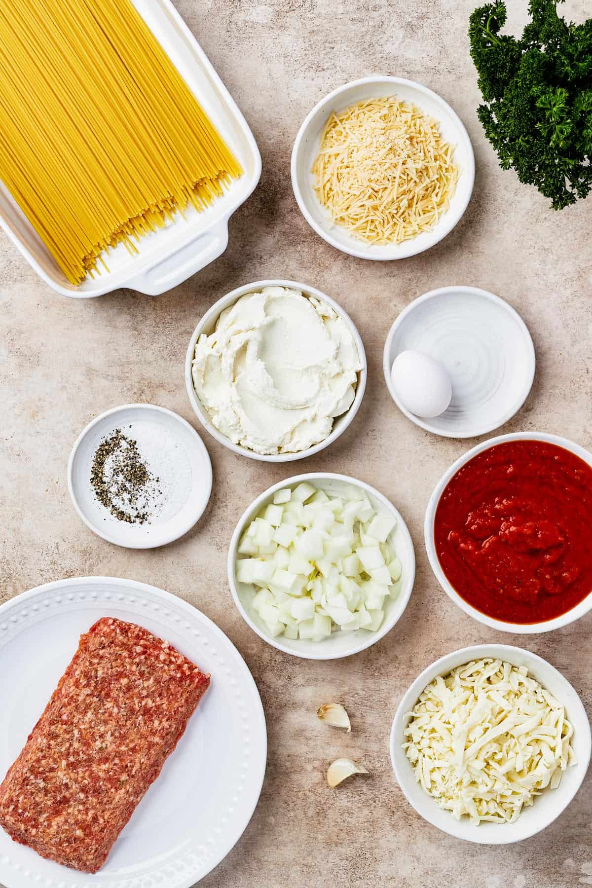 From top left: dry spaghetti, onion, seasonings, ricotta, an egg, mozzarella, marinara sauce, italian sausage, garlic, parmesan.