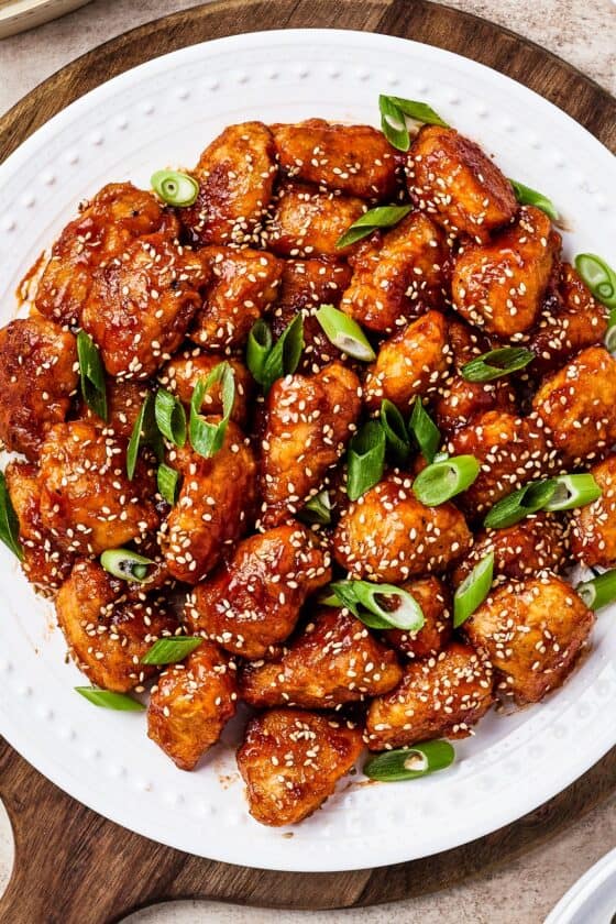 Close-up shot of sweet and sour chicken with rice, green onions, and toasted sesame seeds.