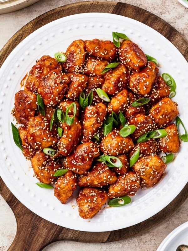 overhead shot of sweet and sour chicken served on a white plate with rice, green onions, and toasted sesame seeds.