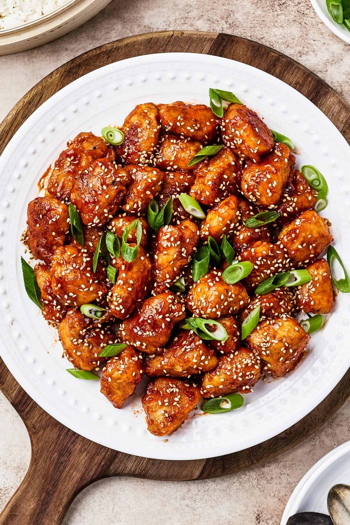 overhead shot of sweet and sour chicken served on a white plate with rice, green onions, and toasted sesame seeds.