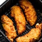 four breaded and cooked chicken tenders arranged inside a black air fryer basket.