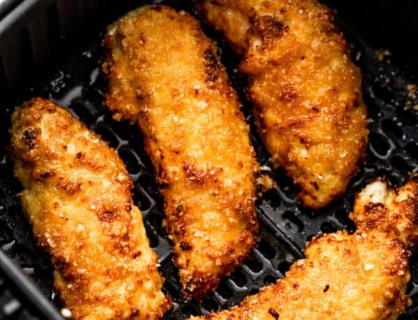 four breaded and cooked chicken tenders arranged inside a black air fryer basket.