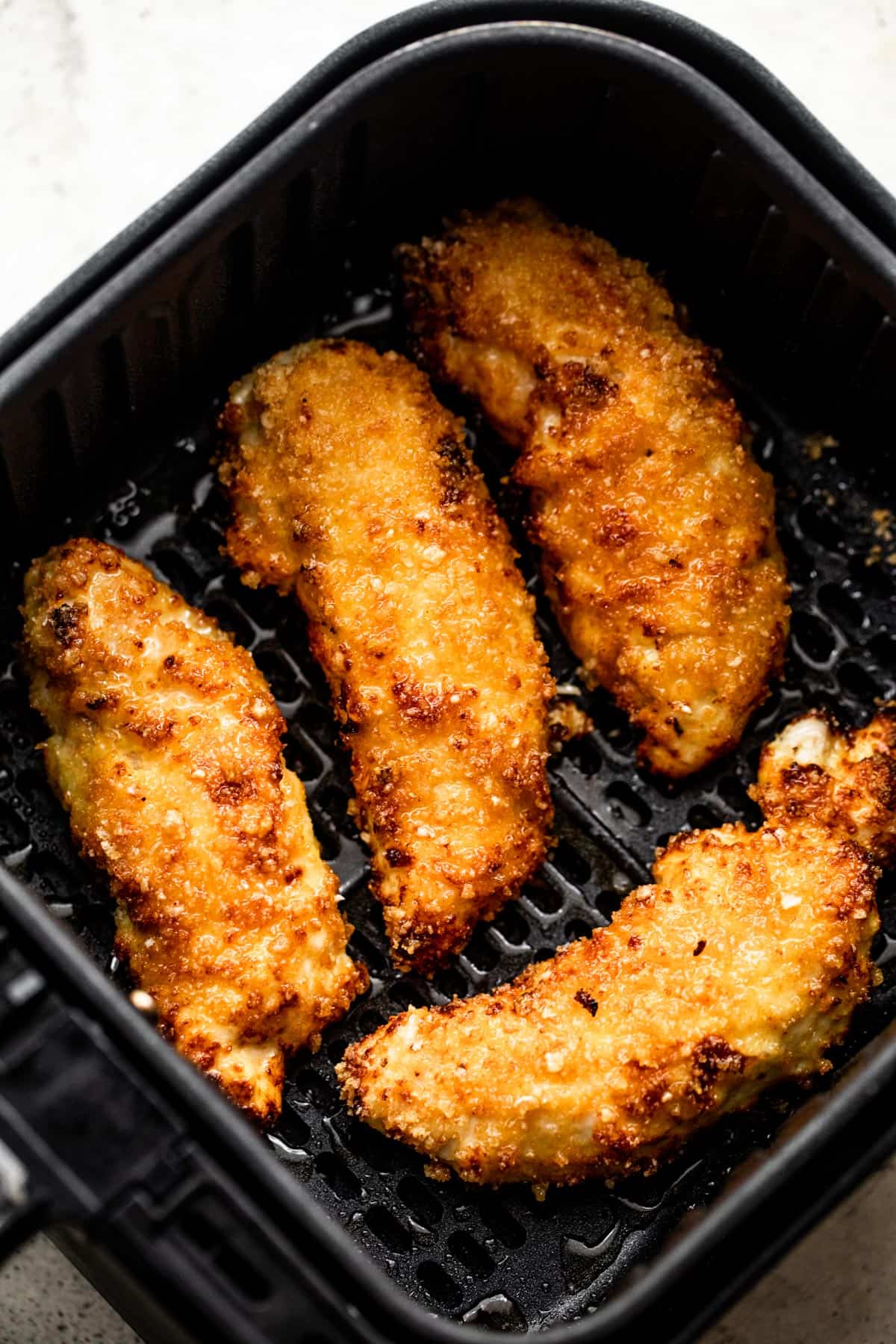 four breaded and cooked chicken tenders arranged inside a black air fryer basket.