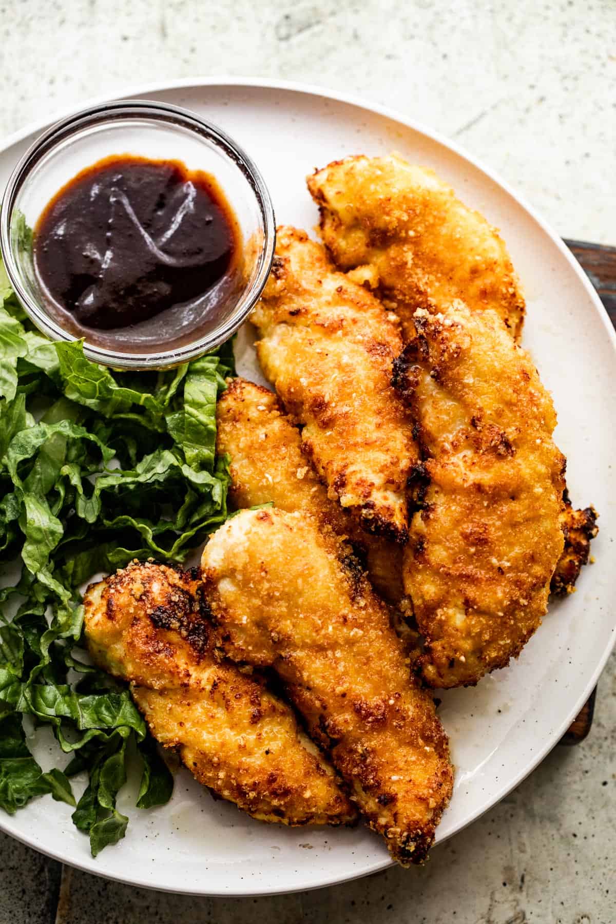 overhead shot of a dinner plate with chicken tenders, greens, and bbq sauce.