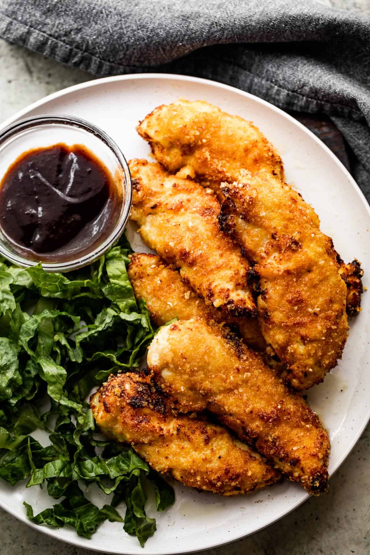 a dinner plate with chicken tenders, greens, and bbq sauce.