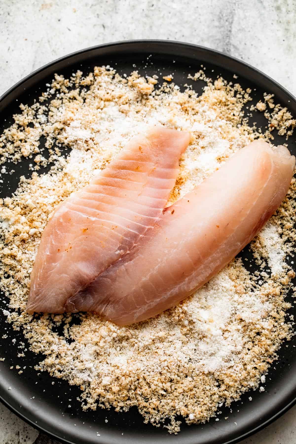 raw tilapia filet placed on top of parmesan bread crumb mixture
