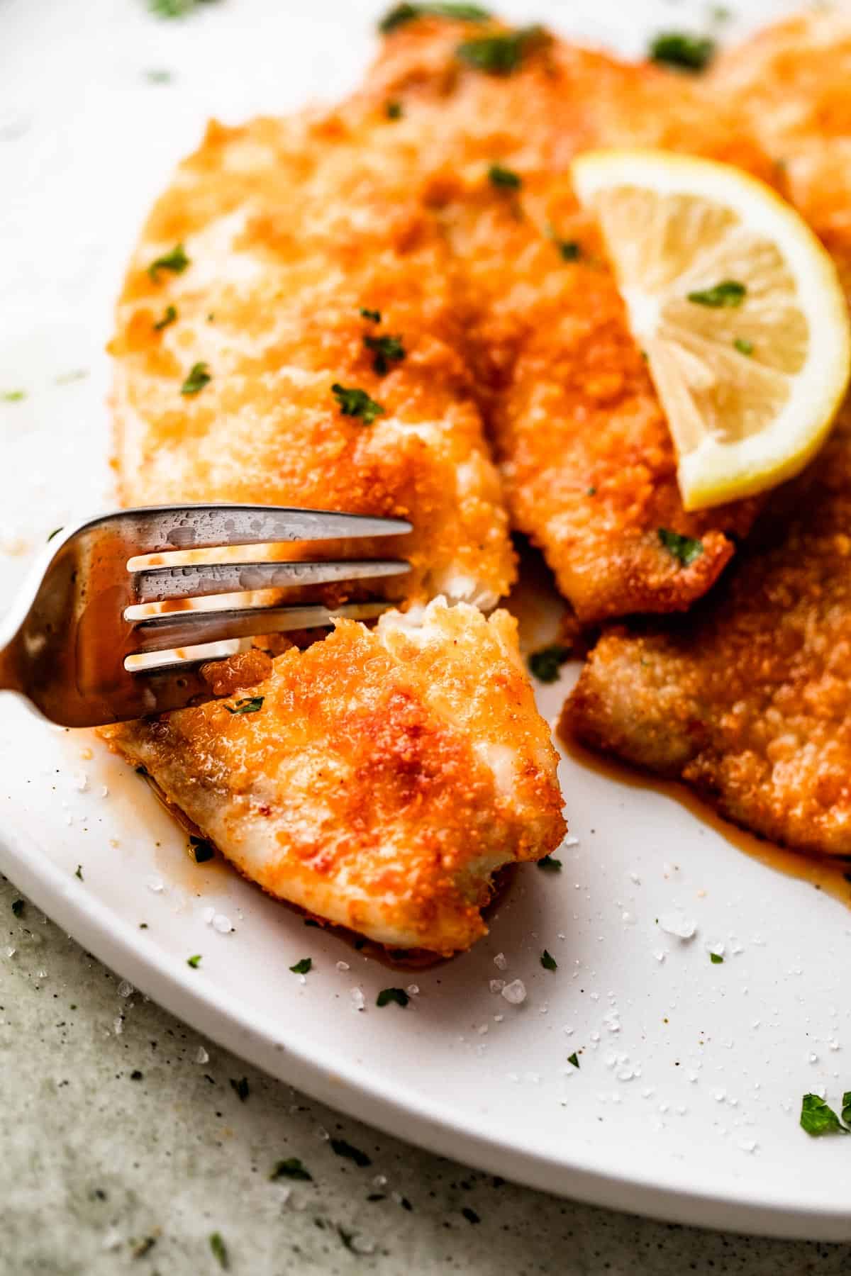 a fork cutting through air fryer parmesan crusted tilapia.