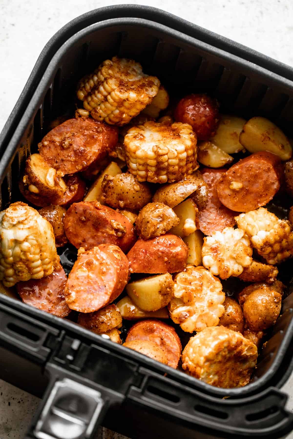 overhead shot of corn on the cob rounds, andouille sausage rounds, shrimp, and potatoes inside of a black air fryer basket.