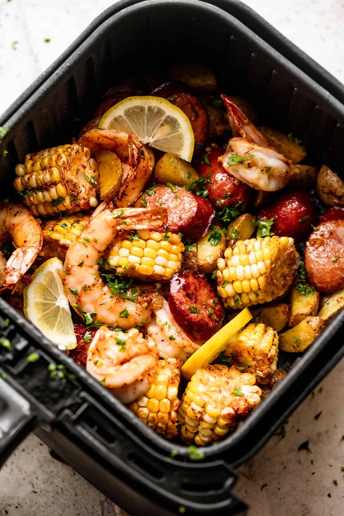 overhead shot of corn on the cob rounds, andouille sausage rounds, shrimp, and lemon slices inside of a black air fryer basket.