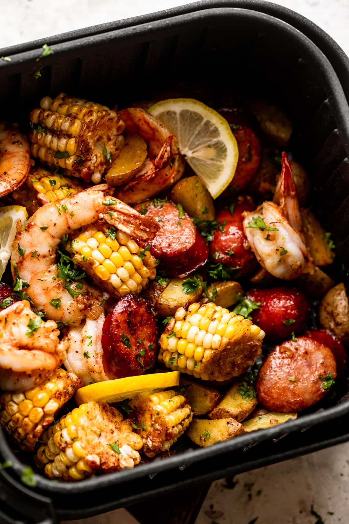 overhead shot of corn on the cob rounds, andouille sausage rounds, shrimp, and lemon slices inside of a black air fryer basket.