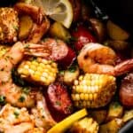 close up shot of corn on the cob rounds, andouille sausage rounds, shrimp, and lemon slices inside of a black air fryer basket.