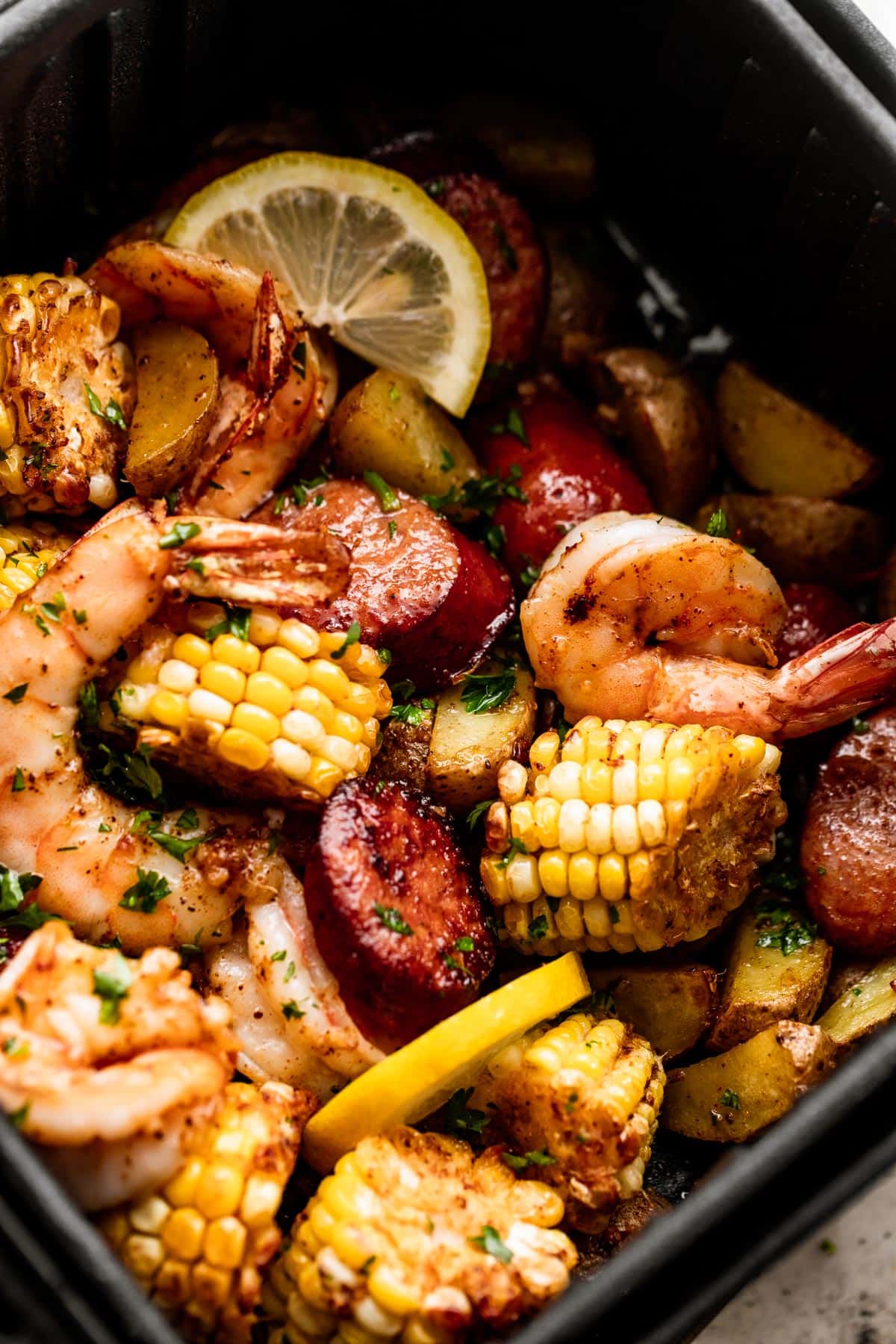 close up shot of corn on the cob rounds, andouille sausage rounds, shrimp, and lemon slices inside of a black air fryer basket.