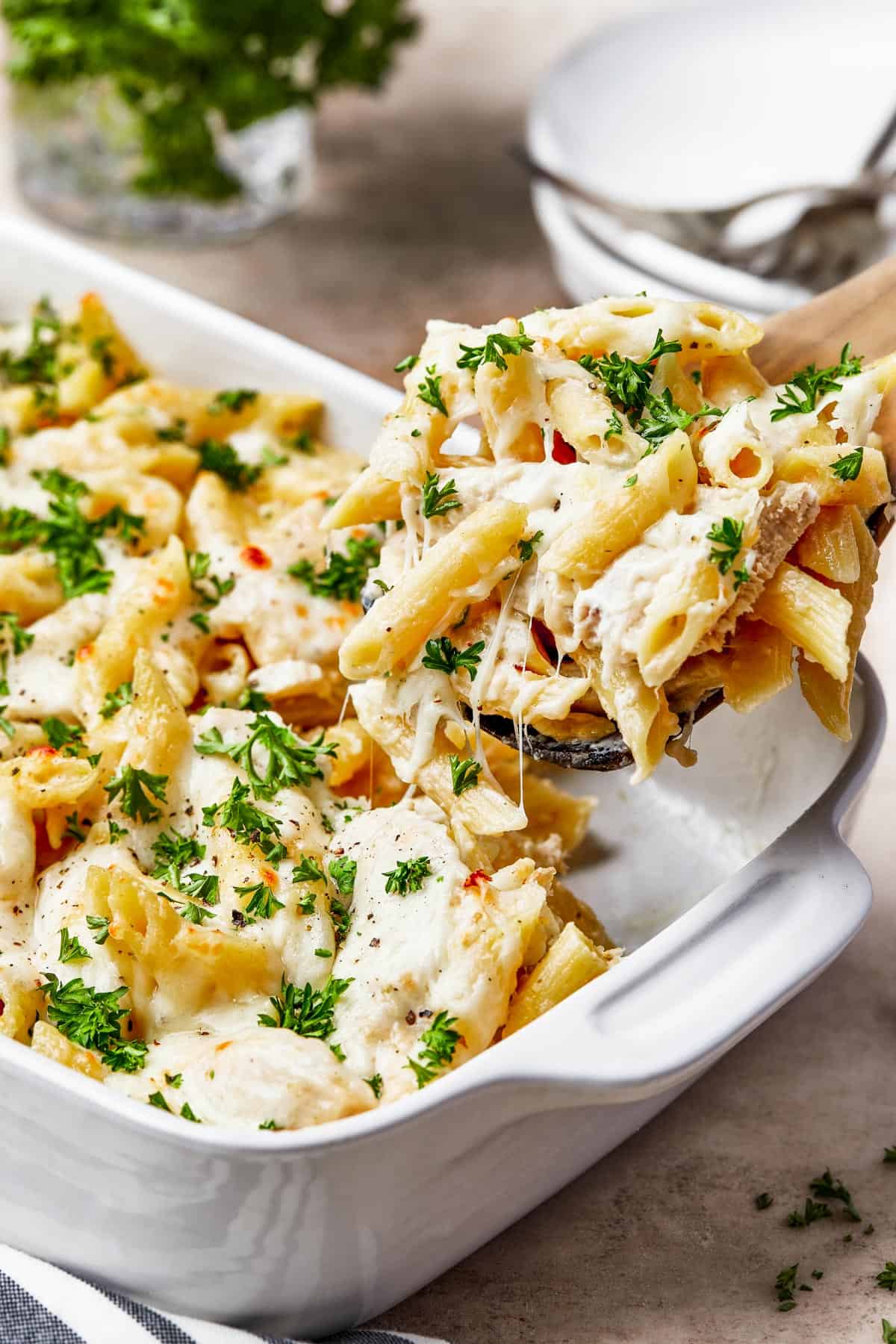 Chicken alfredo pasta being scooped out of a casserole dish.