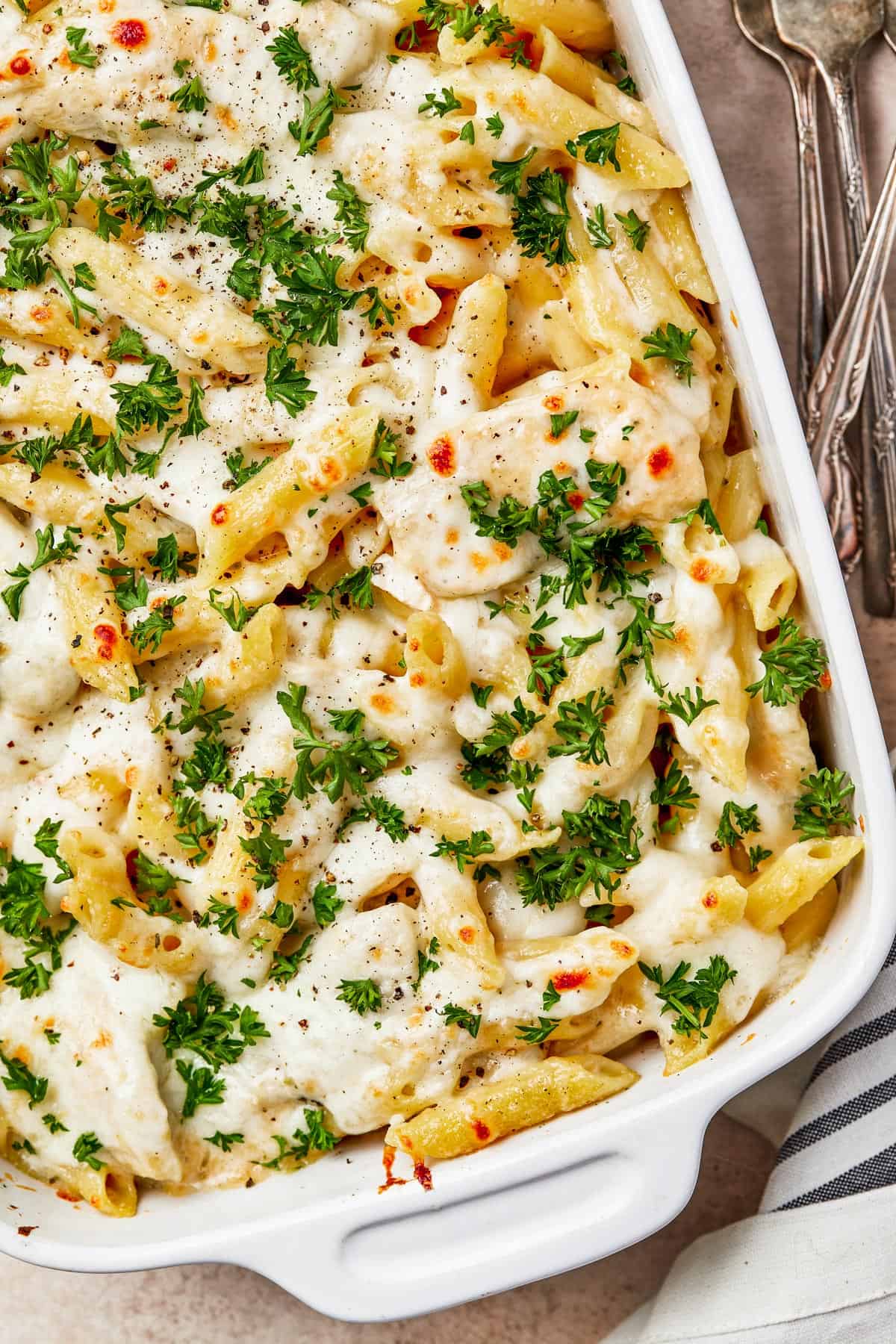 A baked chicken and pasta casserole, generously garnished with parsley.