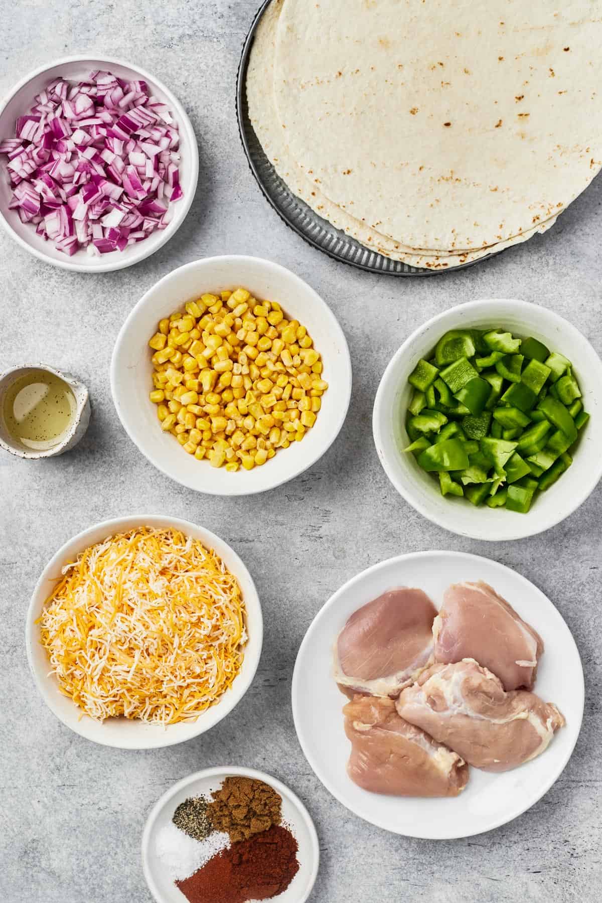 From top left: Red onion, tortillas, oil, corn kernels, bell pepper, cheese, chicken thighs, spices.