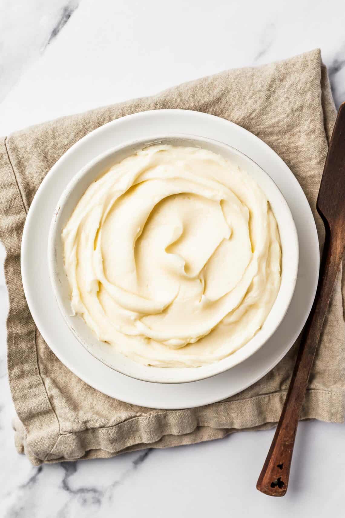 A bowl of creamy white icing on a linen napkin.