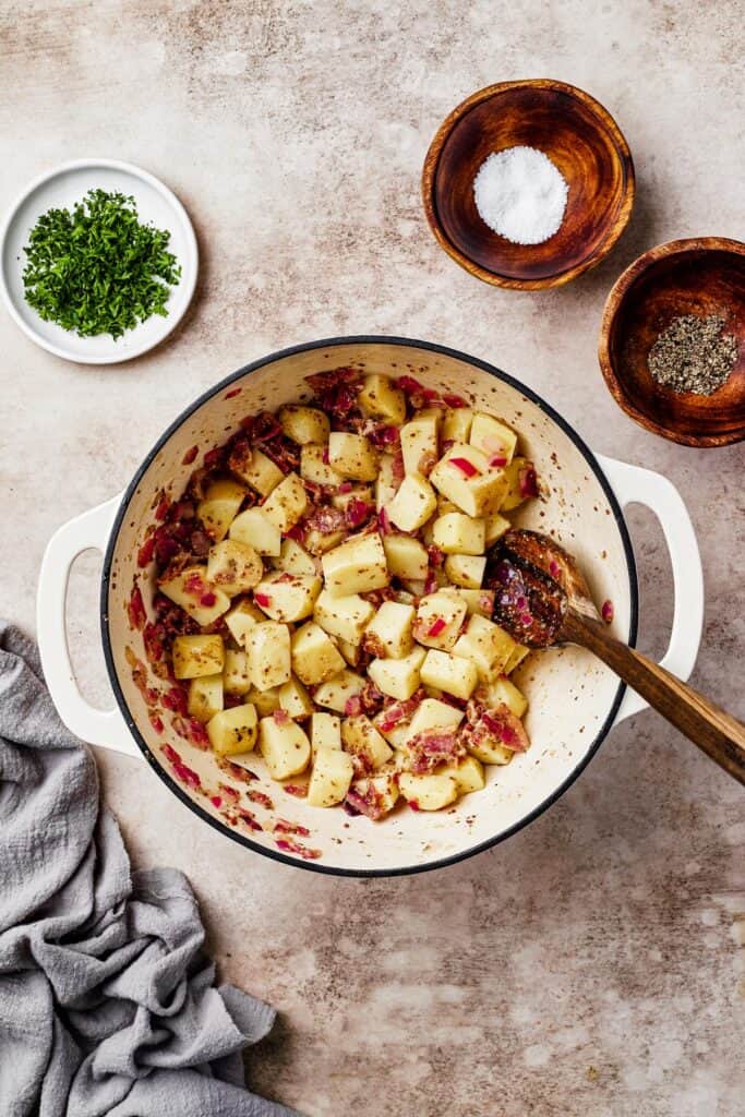 Potatoes mixed with bacon and other ingredients in a large pot.