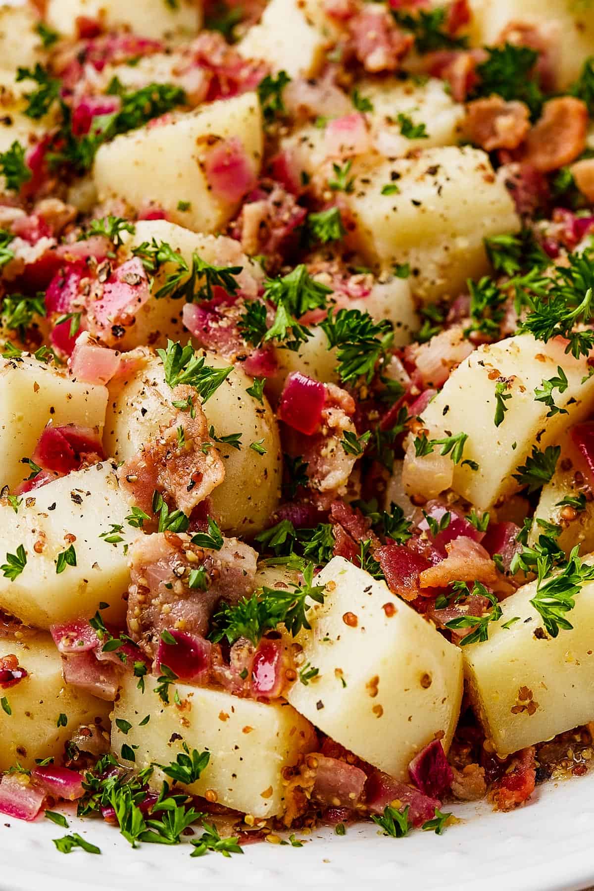 Close-up shot of potato salad on a white serving dish.