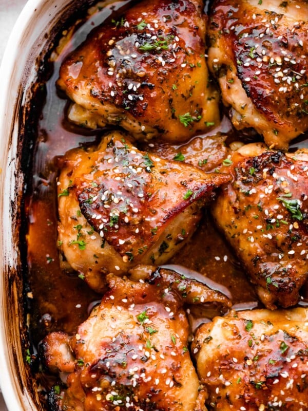 overhead shot of a baking dish with six honey garlic baked chicken thighs garnished with sesame seeds.