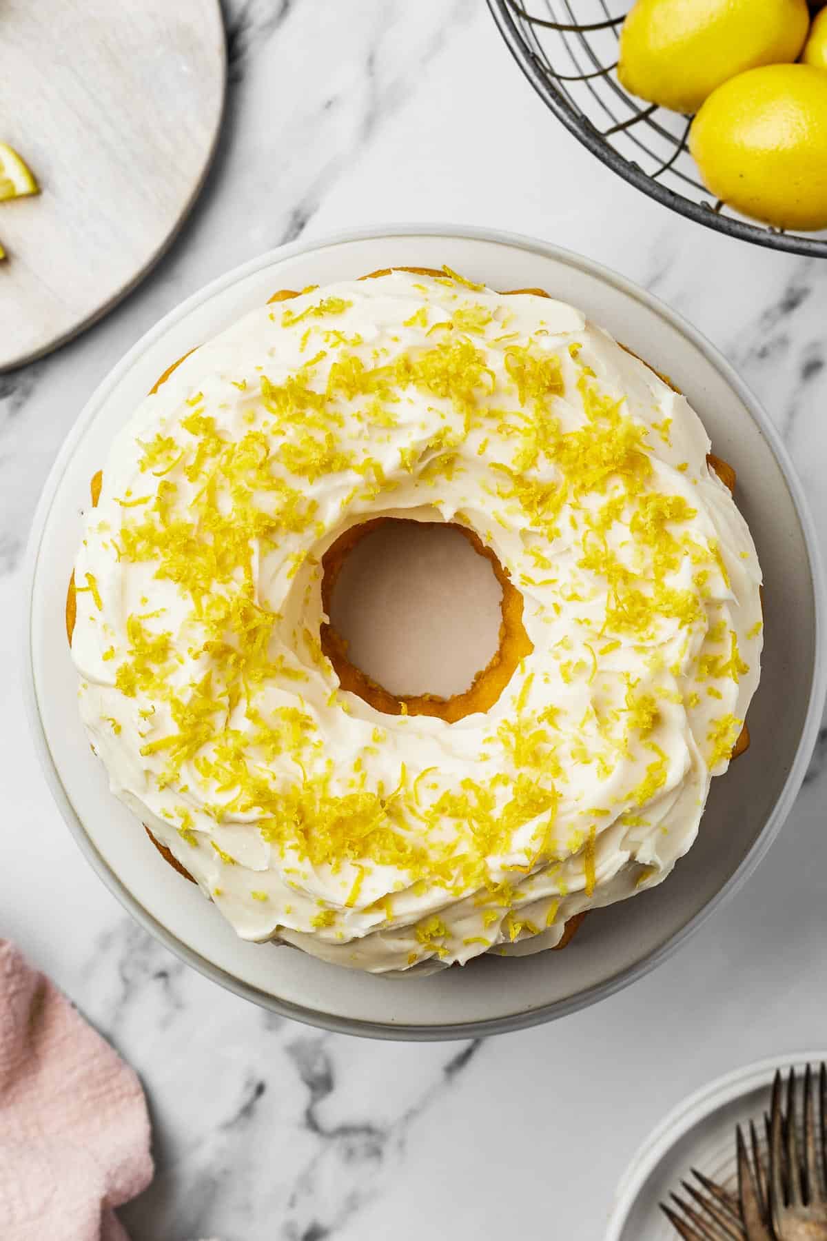 A decorated cake with white frosting and lemon zest on a round white plate.
