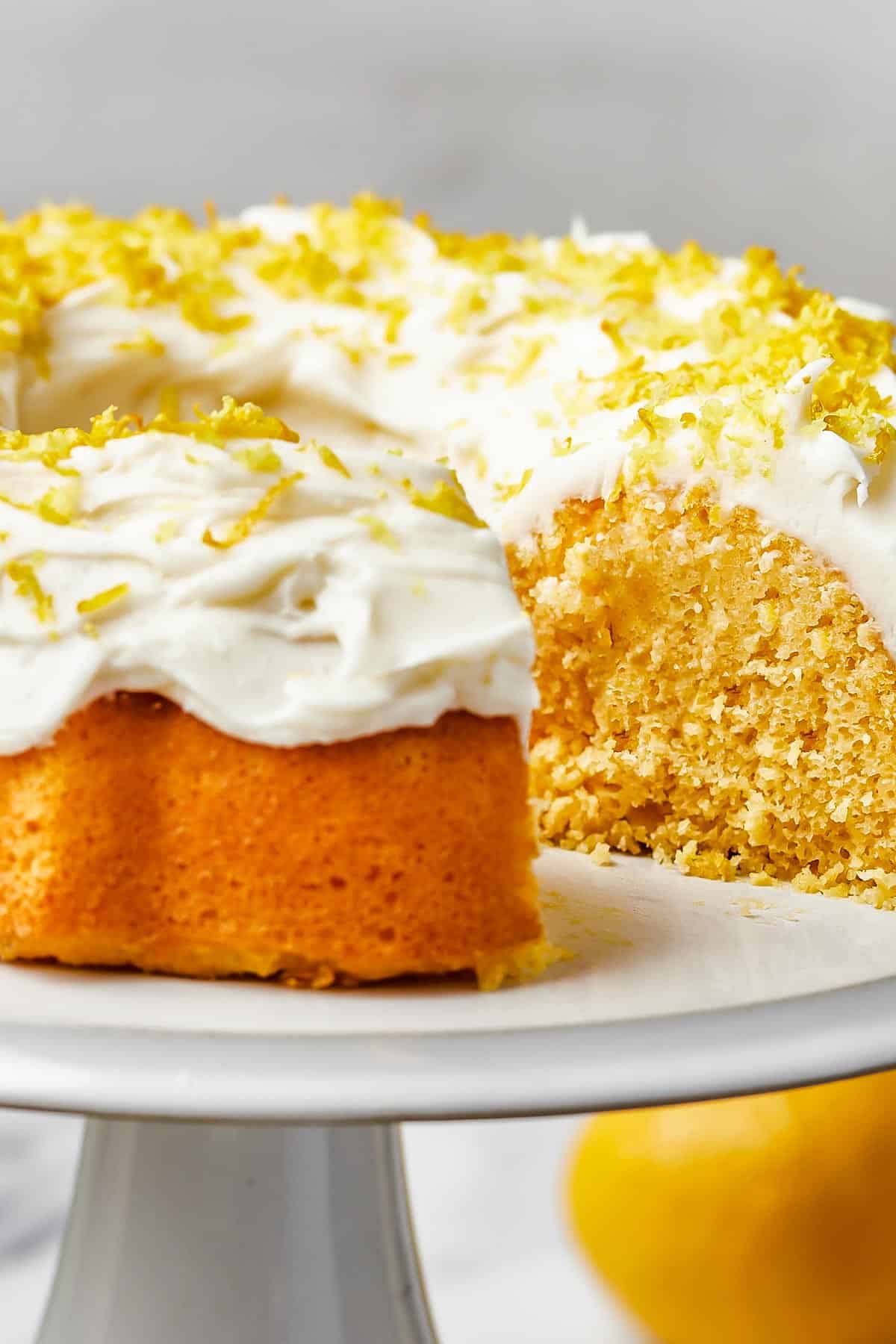 close up shot of a bundt cake iced with thick, creamy frosting and topped with lemon zest.