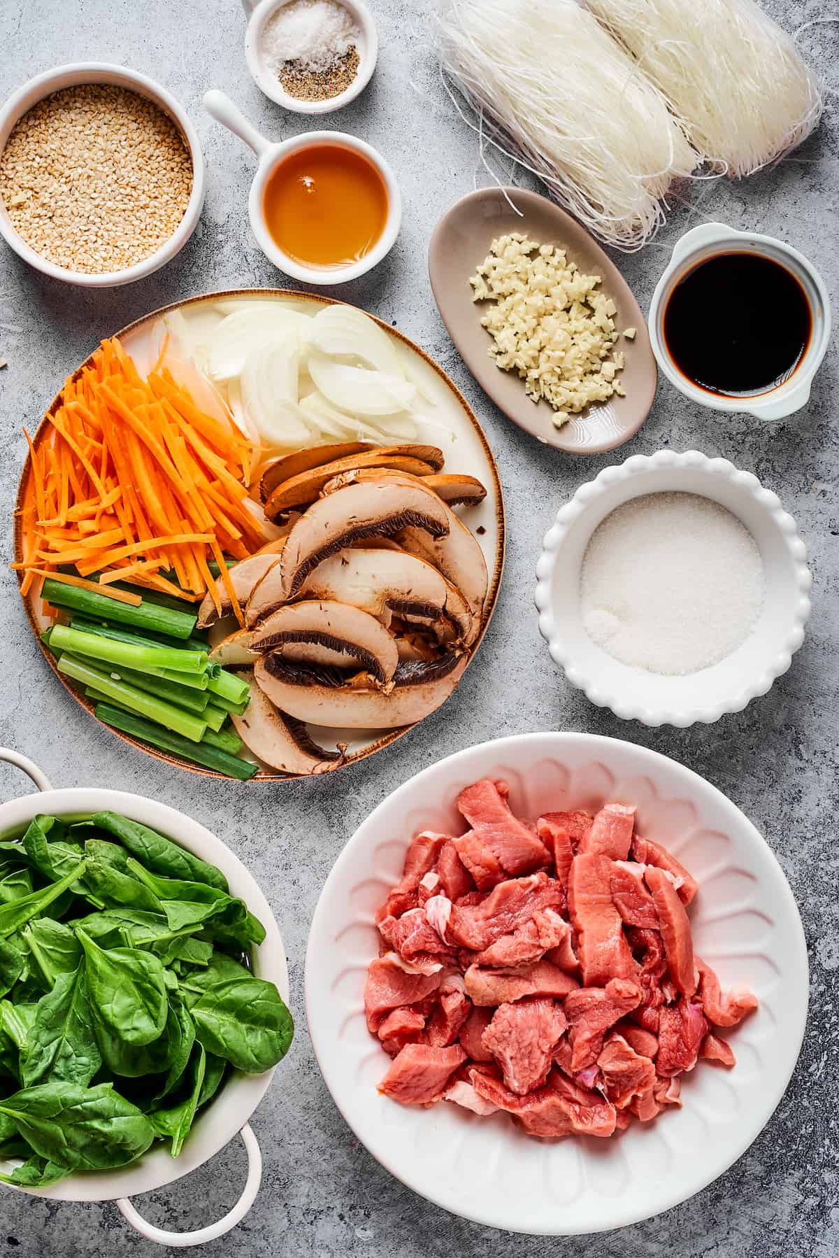 From top left: Toasted sesame seeds, salt and pepper, dried glass noodles, sesame oil, garlic, soy sauce, carrots, onions, green onion, mushrooms, sugar, spinach, sliced steak.