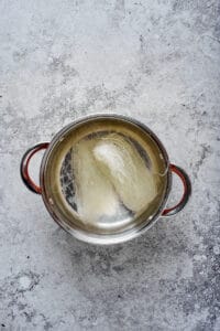 Glass noodles rehydrating in a stainless steel pot of hot water.