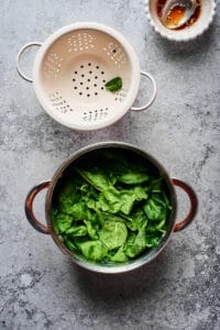 A pot of blanched spinach next to a colander for draining.
