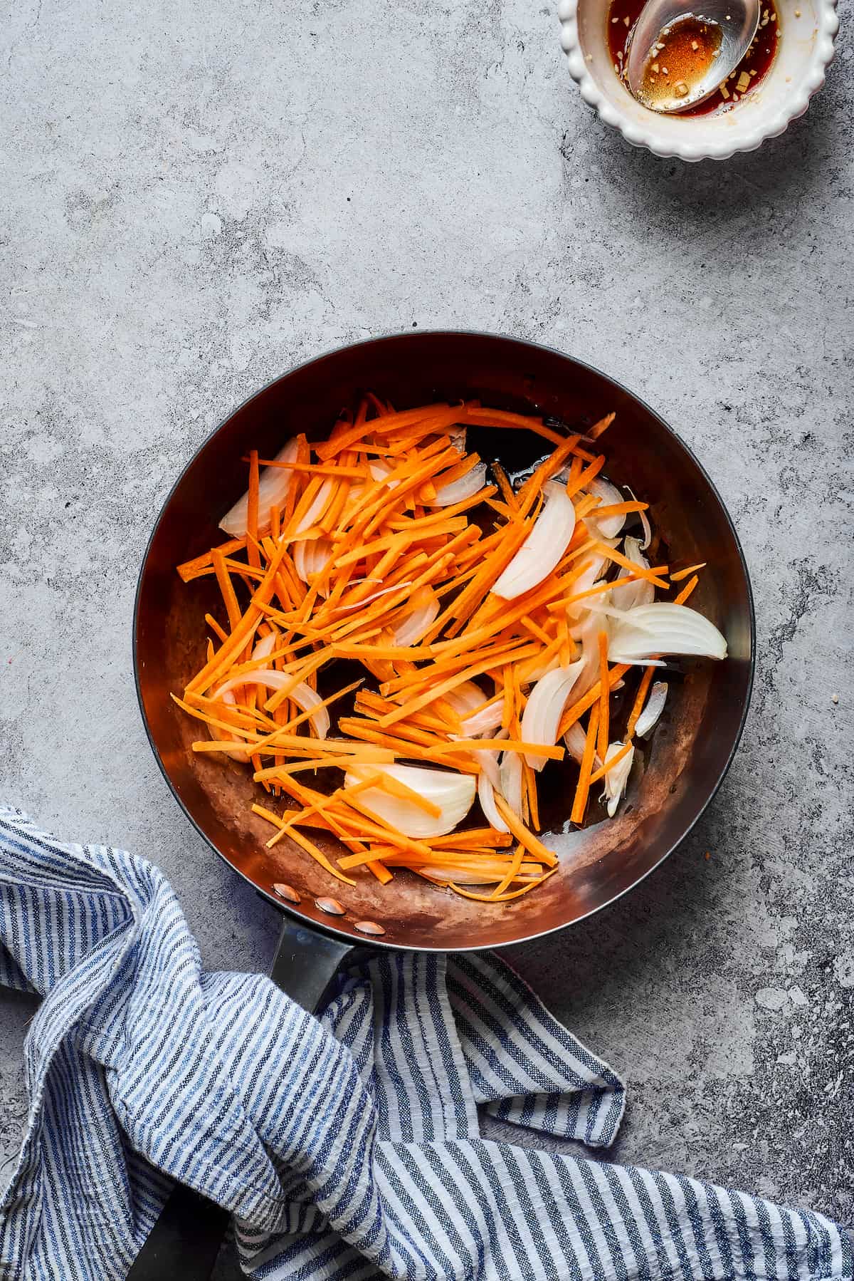 Matchstick carrots and sliced onions in a skillet.
