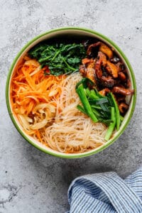 A large bowl with glass noodles, beef, mushrooms, green onions, carrots, and spinach.