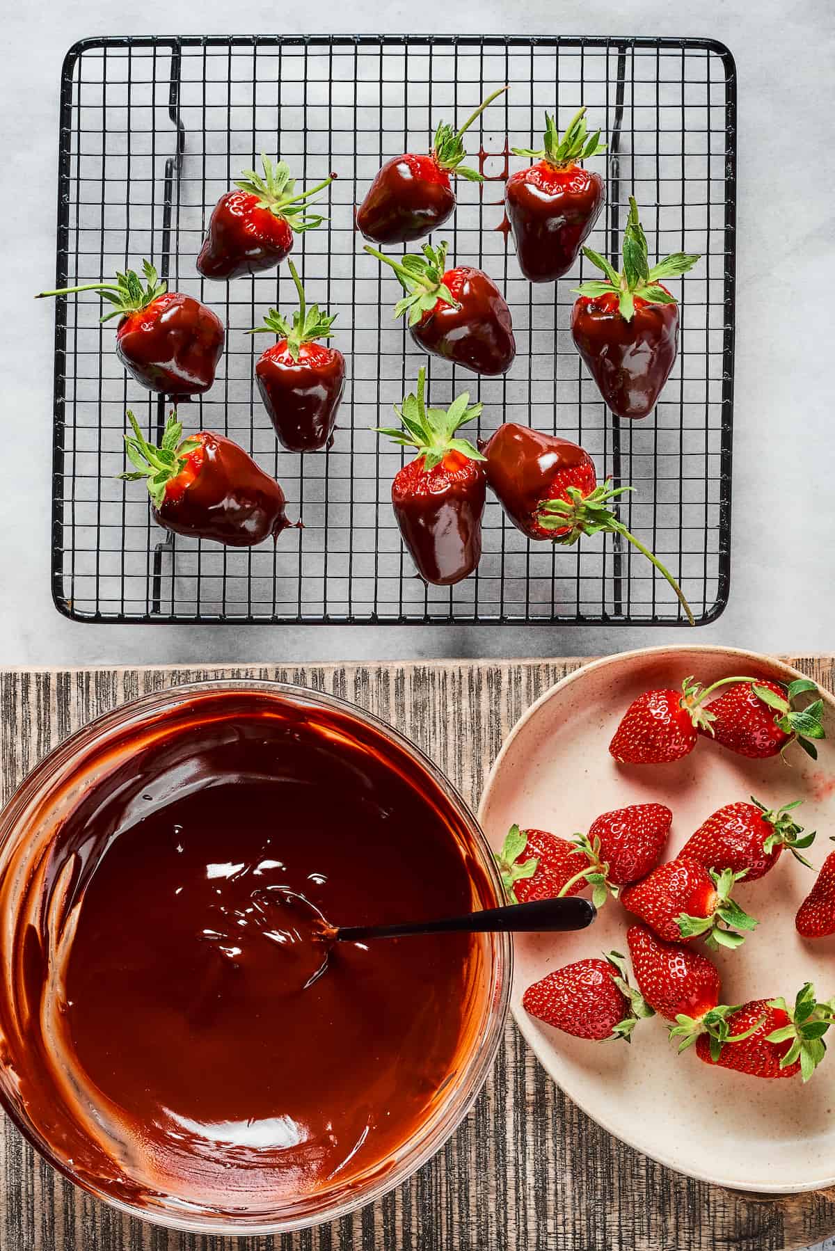 strawberries, melted chocolate, and a wire rack with dipped strawberries resting on it.