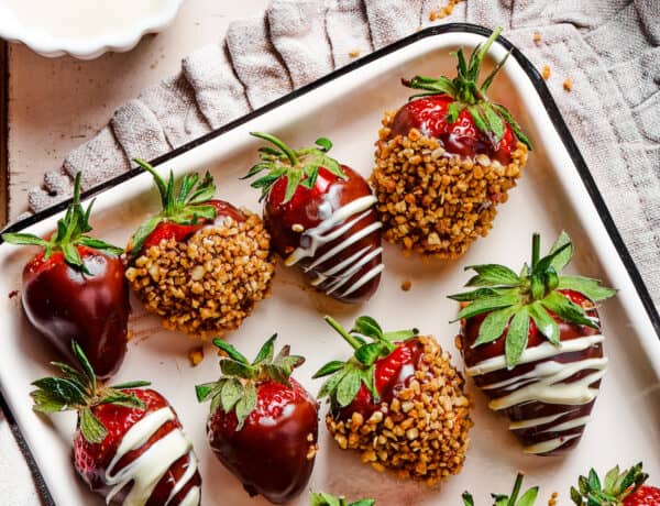 A white tray with a black border, displaying three kinds of chocolate dipped strawberries: plain, white chocolate drizzle, and toasted hazelnuts.
