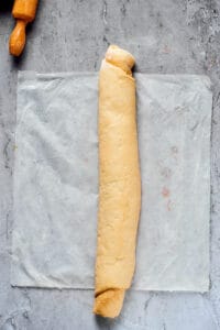 A long, rolled-up piece of yeast dough on a sheet of parchment, next to a rolling pin.