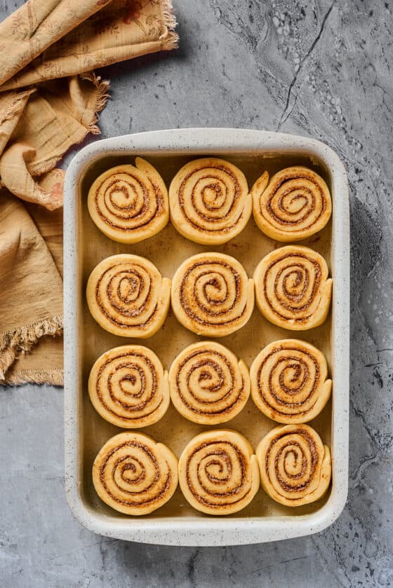 Sliced, unbaked cinnamon buns, lined up in a metal baking dish.