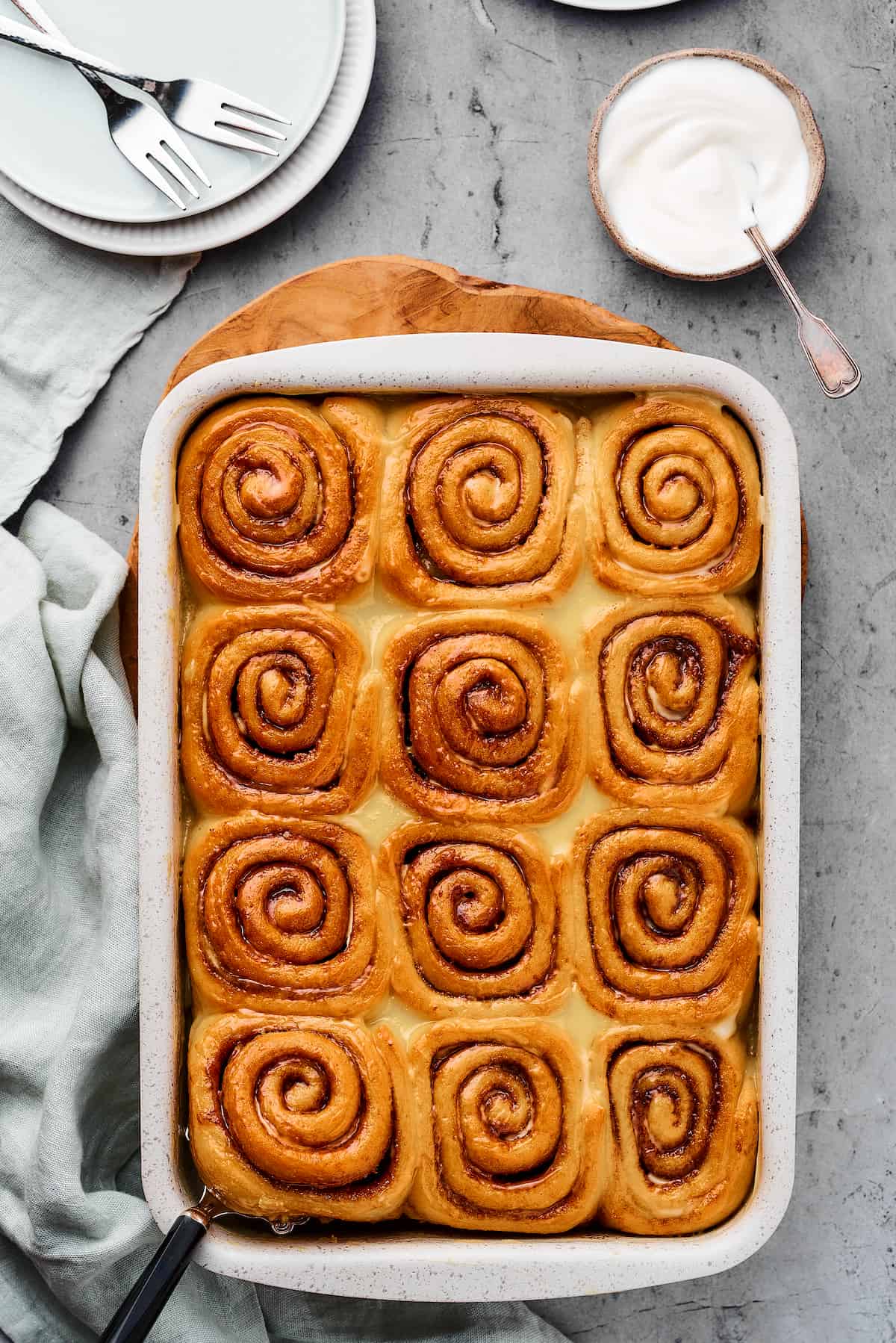 Baked cinnamon rolls in a baking pan, with a cloth dishtowel nearby.