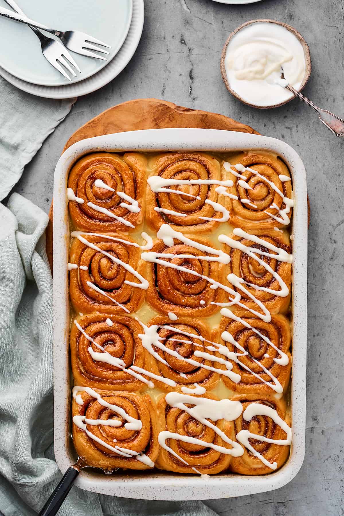 A pan of baked cinnamon rolls drizzled with icing.