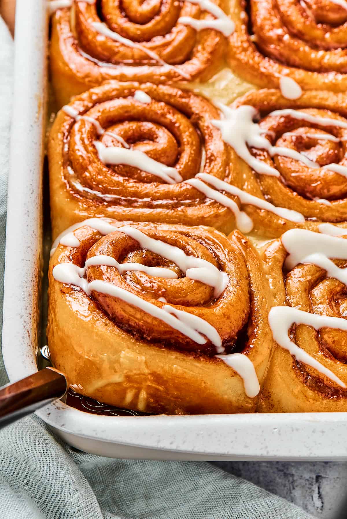 A pan of sticky homemade cinnamon buns. One is being lifted from the corner of the pan with a metal spatula.