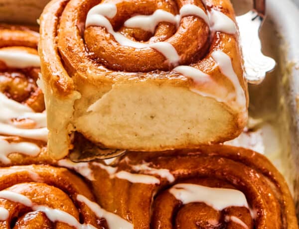 A cinnamon bun lifted from a pan, to show the texture of the torn side of the roll.