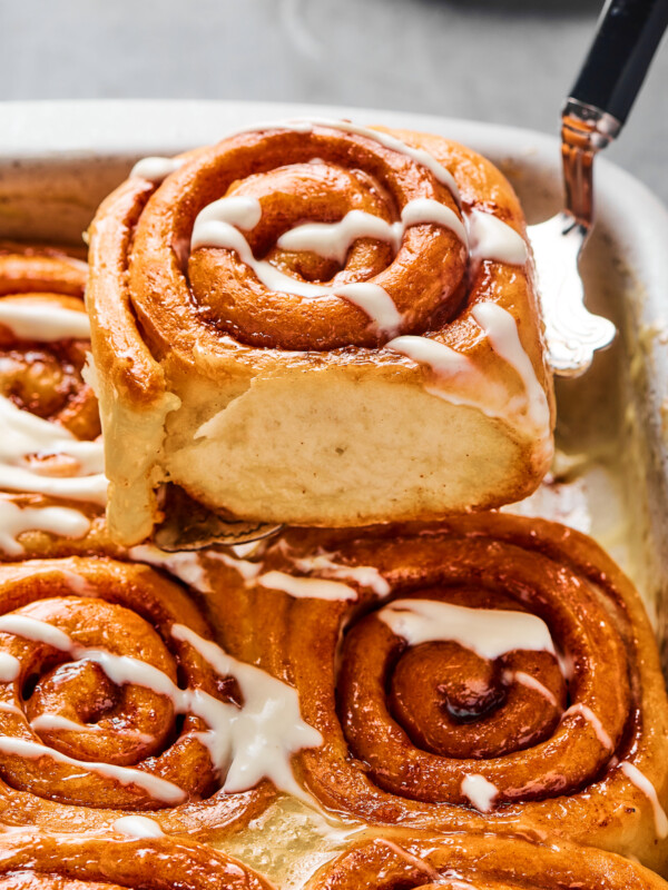 A cinnamon bun lifted from a pan, to show the texture of the torn side of the roll.