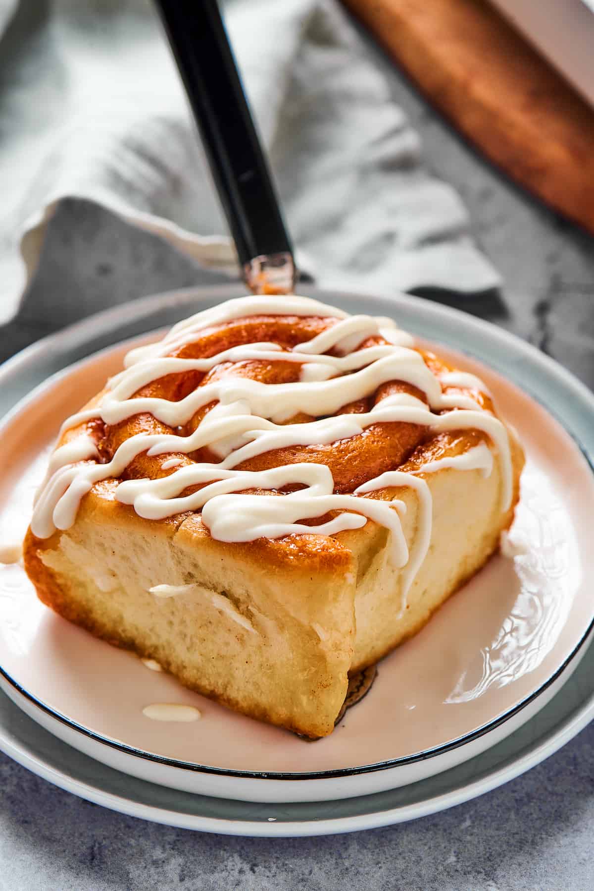 A fresh cinnamon bun on a small plate, with thick white glaze drizzled on top.