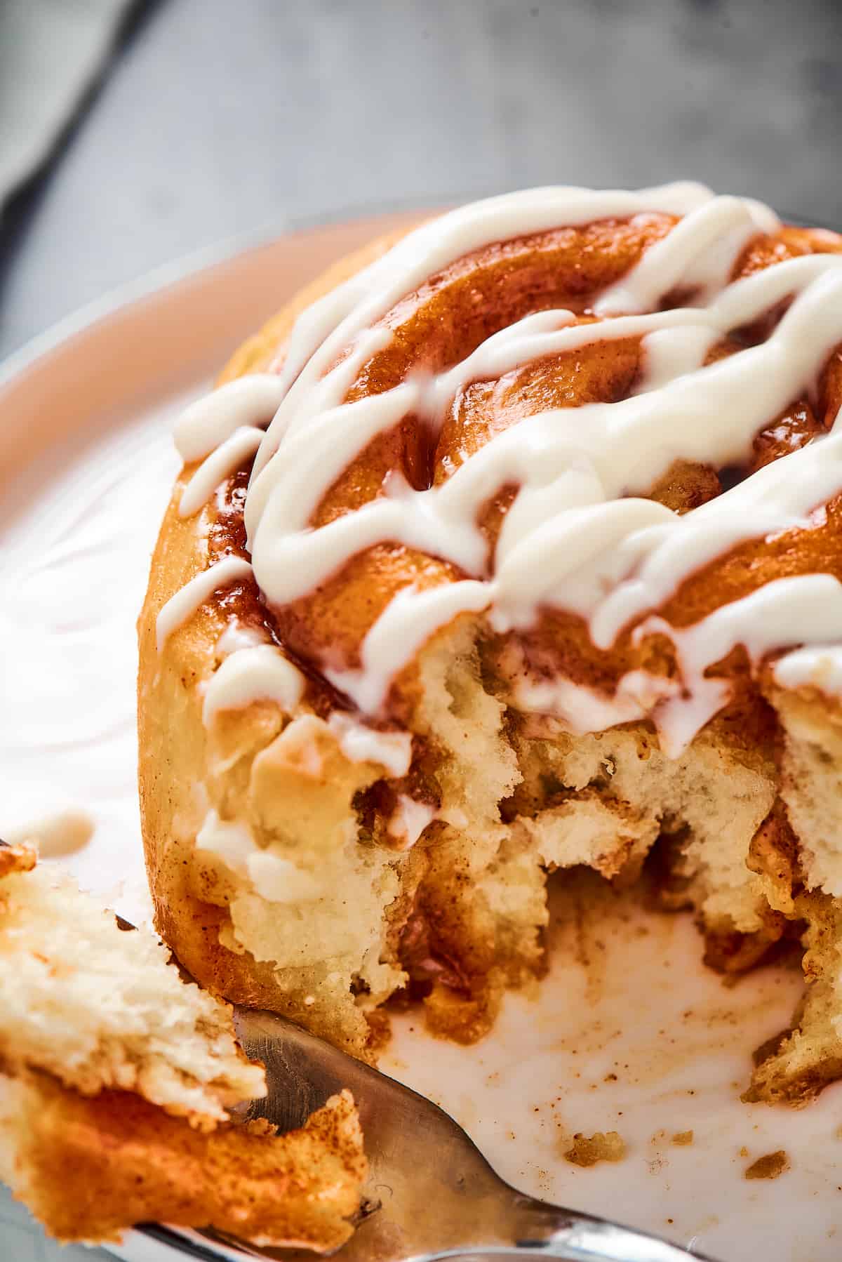 A fresh cinnamon roll with a bite taken from it, on a small plate.