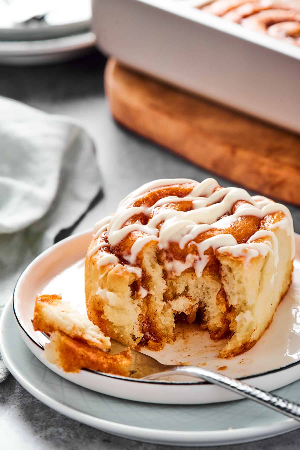 A bitten cinnamon bun on a small plate with a fork.
