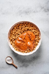 A large mixing bowl of Chex cereal, with a melted peanut butter chocolate mixture poured on top.