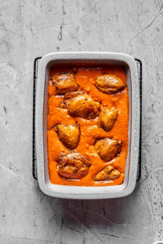 A baking dish full of creamy tomato peanut sauce, with chicken thighs arranged in the sauce.