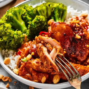 A close-up shot of a chicken thigh cooked in peanut sauce, with a fork pulling away a bite.