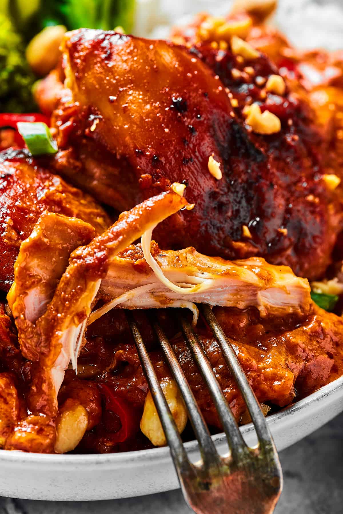 A close-up shot of a chicken thigh cooked in peanut sauce, with a fork pulling away a bite.