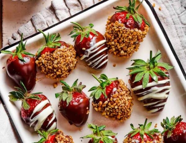 A white tray with a black border, displaying three kinds of chocolate dipped strawberries: plain, white chocolate drizzle, and toasted hazelnuts.